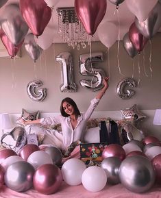 a woman sitting on top of a bed surrounded by balloons and streamers in the shape of numbers