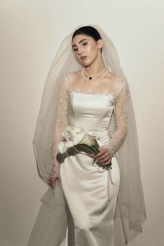 a woman in a white wedding dress holding a bouquet and wearing a long veil over her head