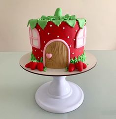 a strawberry themed birthday cake on a white pedestal with a pink house in the background