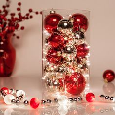 a vase filled with red and silver ornaments on top of a white table next to other christmas decorations