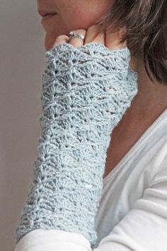 a woman is wearing a crocheted arm warmer in light blue and has her hand on her face