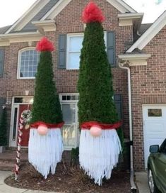 two tall trees with red bows on their heads are in front of a brick house