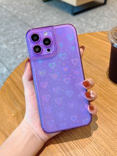 a person holding up a purple phone case with hearts on it and a cup of coffee in the background