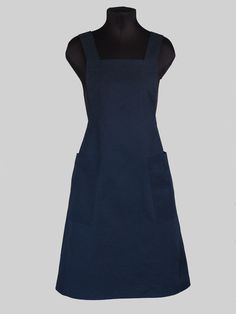 the apron dress is made from dark blue cotton and features an adjustable neckline, two pockets, and a front pocket