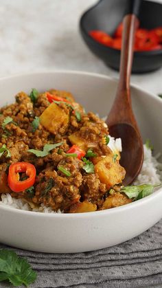 a white bowl filled with rice and meat on top of a table next to a wooden spoon