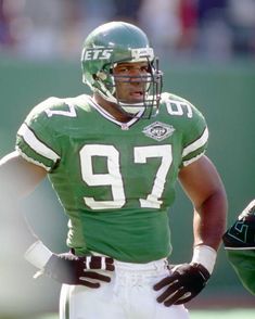 a football player standing on the field with his hands in his pockets and wearing a green uniform