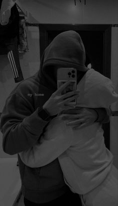 a man in a hoodie taking a selfie with his cell phone while standing in front of a mirror