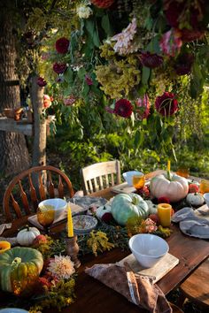 a wooden table topped with plates and bowls covered in flowers next to a bunch of pumpkins