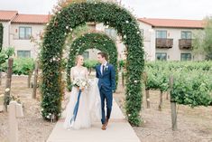 the bride and groom are walking down the path in front of an arch covered with flowers