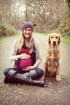 a pregnant woman sitting on the ground next to her dog, with trees in the background