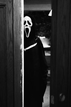 a person wearing a ghost mask standing in front of a door with their mouth open