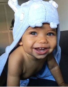 a smiling baby wearing a blue towel on top of his head