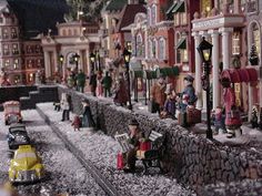 a toy train set with people and cars on the tracks