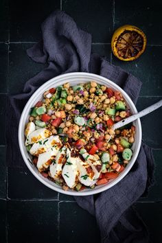 a white bowl filled with salad next to an orange on top of a black table