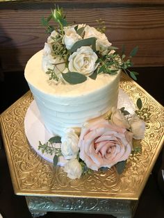 a three tiered cake with white frosting and pink flowers on a gold platter