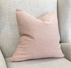 a light pink pillow sitting on top of a gray couch next to a white chair