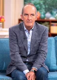 a man sitting on top of a blue couch in front of a tv screen and looking at the camera