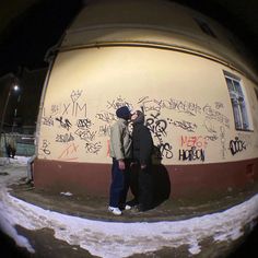 two people standing next to each other in front of a building with graffiti on it