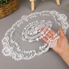 a hand holding a white lace doily on top of a gray surface next to a basket