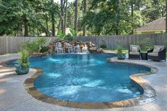 an outdoor pool with waterfall and lounge chairs in the back yard, surrounded by trees