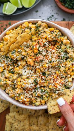 a hand holding a tortilla chip and dipping it into a bowl filled with corn salsa