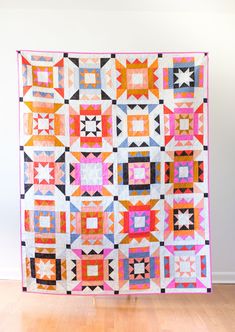 a colorful quilt hanging on the wall in front of a wooden floor and white walls