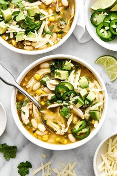 three bowls filled with chicken tortilla soup and topped with shredded cheese, avocado, cilantro, jalapenos, and lime