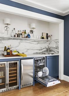 an open dishwasher in the middle of a kitchen with blue cabinets and marble backsplash