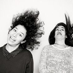 two women standing next to each other with hair flying in the air