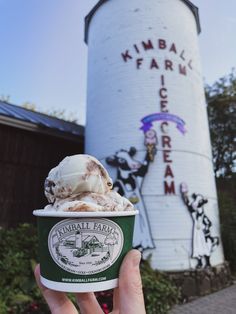 someone is holding up a cup of ice cream in front of a large water tower