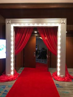 a red carpeted entrance way leading into a room with lights on the walls and curtains