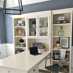 a desk with a laptop computer on top of it next to a book shelf and cabinets