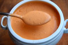 a spoon full of sauce sitting in a white bowl on top of a wooden table