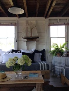 a living room filled with furniture and flowers on top of a wooden table in front of two windows