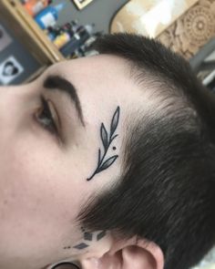 a man with a small tattoo on his forehead and behind his ear is a leaf