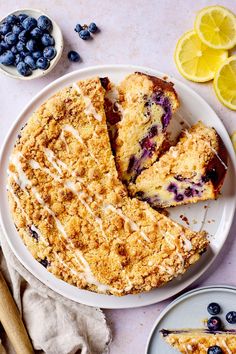 a blueberry crumb cake on a plate with lemons and blueberries around it