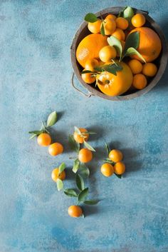 oranges and leaves in a bowl on a blue surface