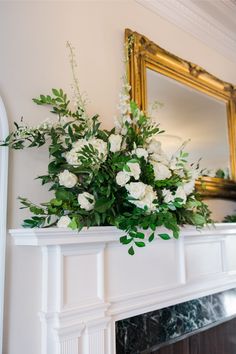 a fireplace mantel decorated with white flowers and greenery