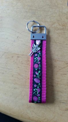 a pink and black keychain with flowers on it sitting on top of a wooden table