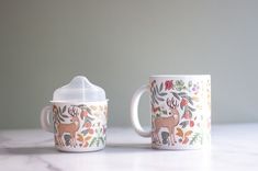 two coffee mugs sitting on top of a white marble counter next to each other