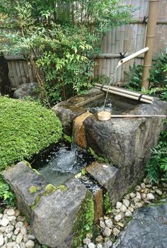 a small garden with rocks and water flowing from the top to the bottom, surrounded by greenery