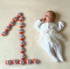 a baby laying on its back next to a number one made out of candies