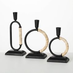 three black and gold candlesticks with rings on them sitting on a white surface