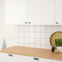 a kitchen with white cabinets and a wooden counter top next to a potted plant