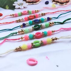 five different colored bracelets on a table with beads and flowers in the back ground