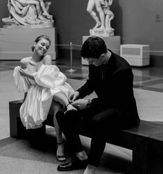 a man kneeling down next to a woman sitting on top of a bench in front of statues