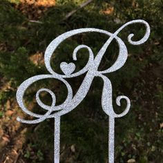 a white cake topper with the letter k on it's side in front of some trees