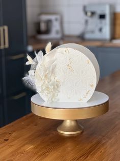 a cake with white flowers and feathers on top of a wooden table in a kitchen