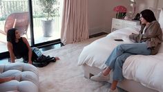 two women sitting on top of a bed in a bedroom next to a sliding glass door