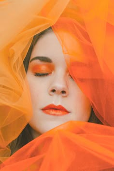 a woman with orange eyeshadow covering her face and veiled over her head